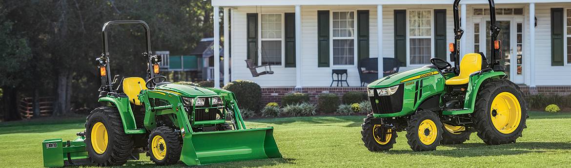 Two green John Deere® tractors parked in front of a lawn.